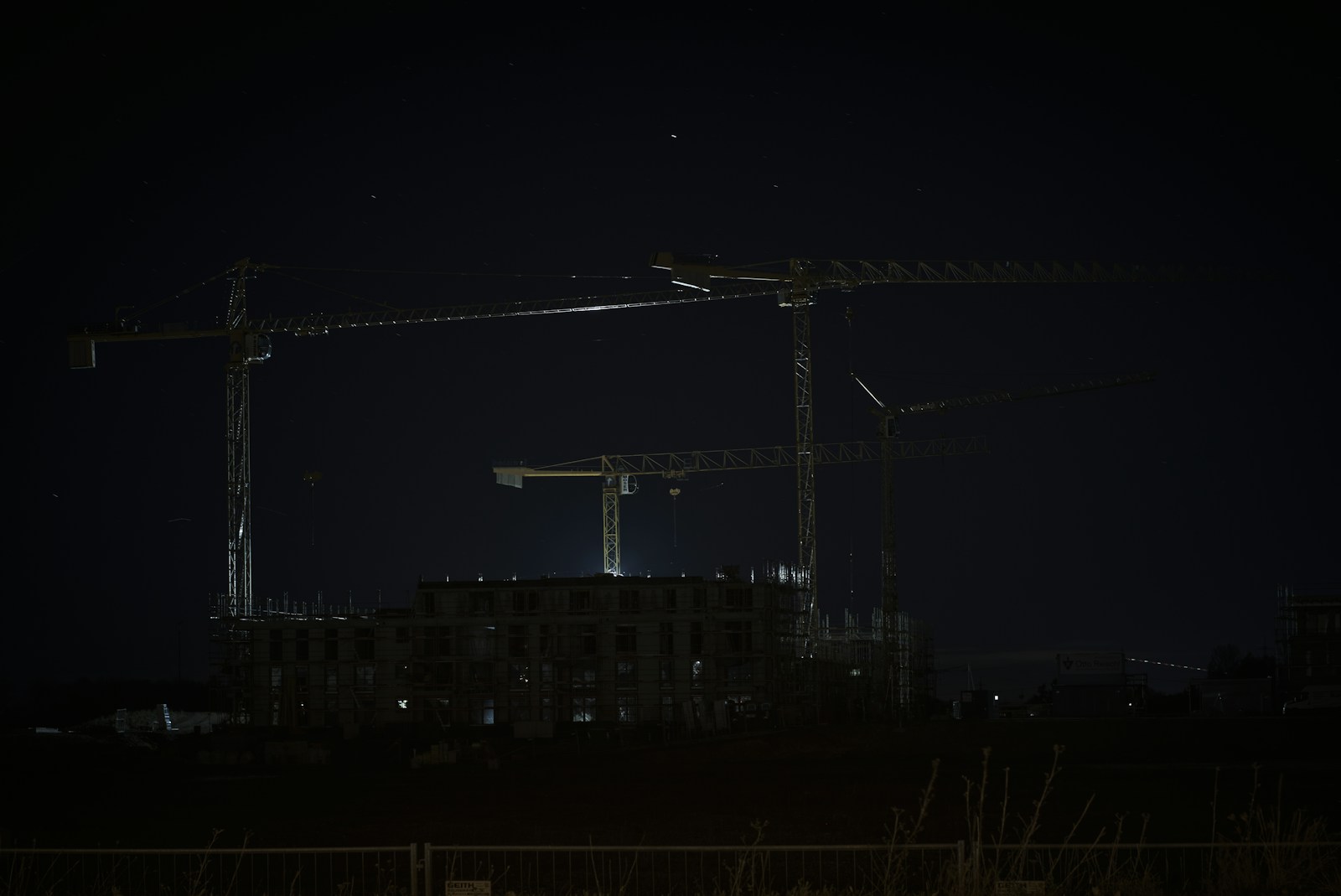 A building under construction at night with a tower crane