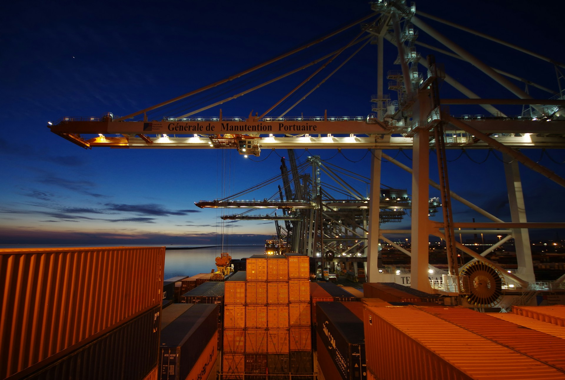 A cargo ship docked at a port at night with its lights on